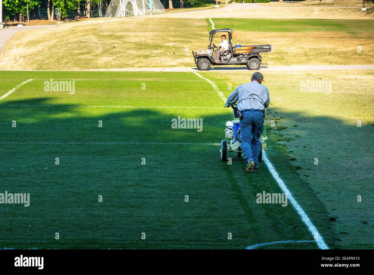 Membre de l'équipe d'entretien de terrain de sport utilisant une machine de peinture au trait sur un terrain de football en Caroline du Nord. Banque D'Images