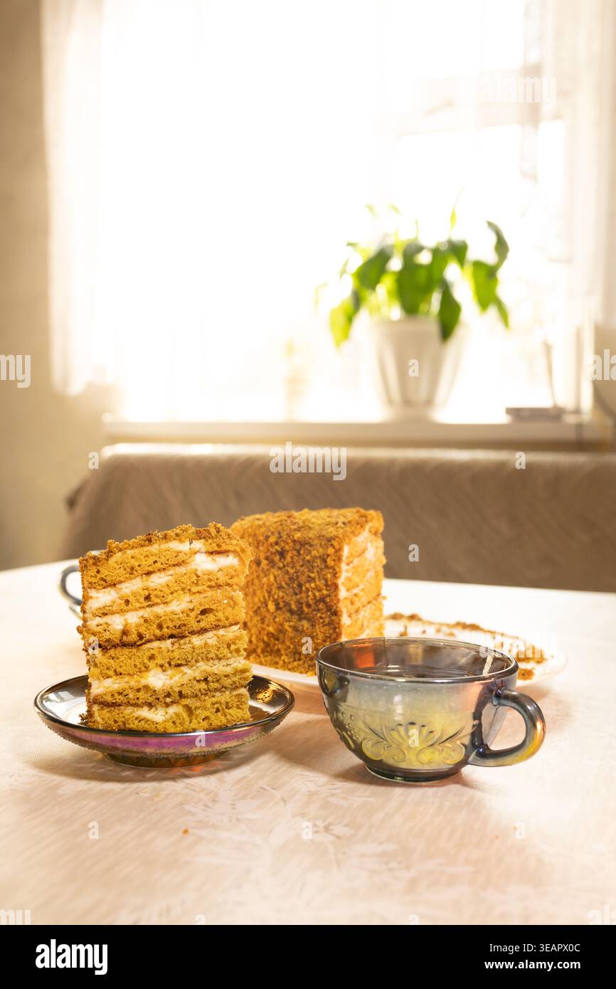 Tranches de gâteau au miel sur la table par fenêtre avec tasse de thé.Cozy photographie de nourriture d'un dessert classique pour les blogs culinaires, les menus de café, et l'annonce de boulangerie maison Banque D'Images