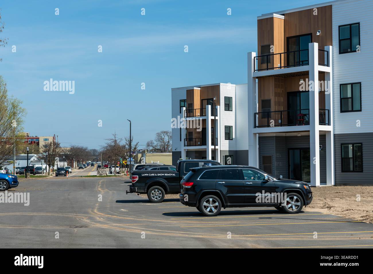 LUDINGTON, MICHIGAN, ÉTATS-UNIS - 23 AVRIL 2026. Le complexe d'appartements Lake District Flats fait face à un parking occupé regardant vers le nord en bas de South James Street à Ludington, Michigan, avec un camion de service d'entretien de pelouse et de déneigement au premier plan et le centre-ville de Ludington visible en arrière-plan, illustrant comment le nouveau développement riverain s'intègre dans le tissu de cette petite ville portuaire de l'ouest du Michigan. Crédit : Jeffrey Wickett/Alamy Live News. Banque D'Images