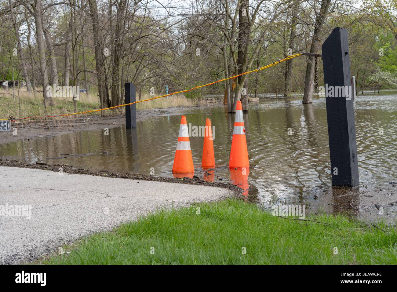 Le sentier du parc a été inondé après de fortes pluies avec des cônes orange et une barrière de marquage d'accès restreint, l'eau couvrant le sol et les arbres dans le backgrou Banque D'Images