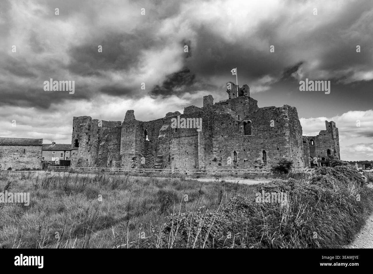 Les ruines du château de Middleham avec le drapeau volant sous le ciel orageux dramatique en noir et blanc Banque D'Images