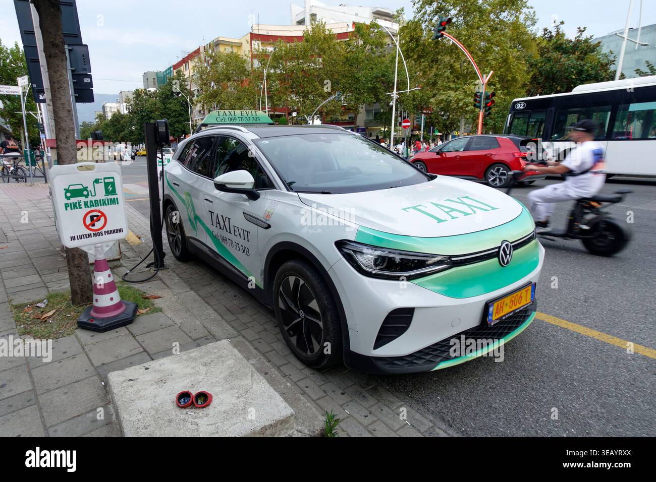 Blanc Volkswagen ID.4 taxi électrique charge à un chargeur côté rue avec texte albanais sur les panneaux dans le paysage urbain de Tirana, Albanie, Europe Banque D'Images