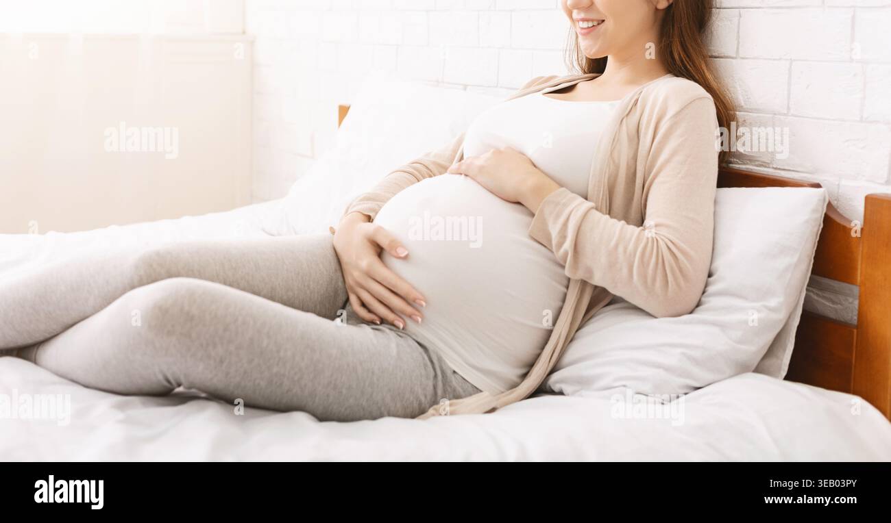 Femme enceinte se relaxant confortablement sur un lit dans une chambre lumineuse et confortable Banque D'Images