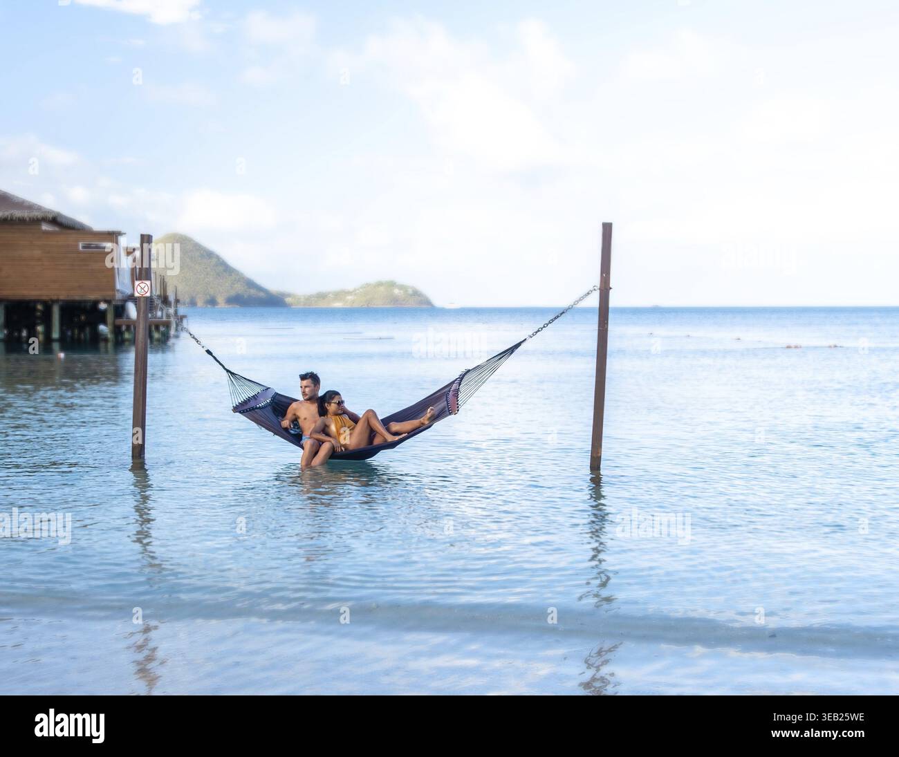 Un couple profite d'un après-midi serein se prélasser ensemble dans un hamac au-dessus des eaux calmes. Un couple multiethnique diversifié d'une femme asiatique et d'un homme caucasien Banque D'Images