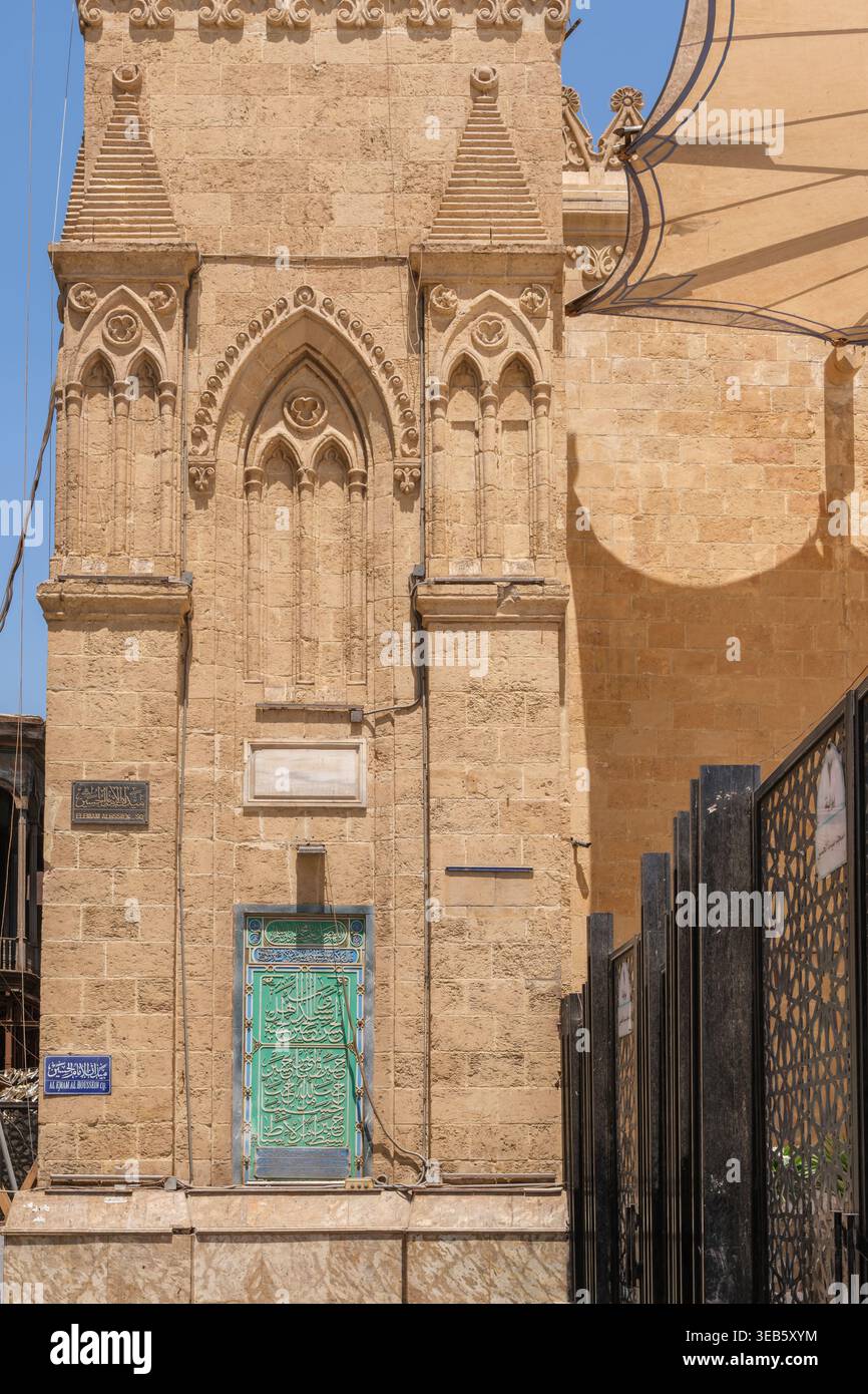Vue sur la mosquée Imam Al-Hussein avec des sculptures en pierre complexes, une porte verte avec calligraphie arabe et une clôture géométrique noire au Caire, EGY Banque D'Images