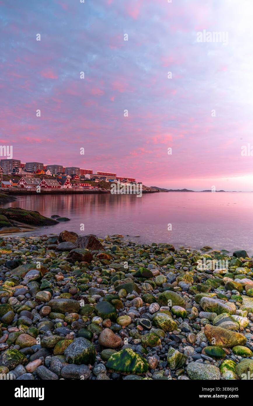 Vue sur la côte rocheuse et les maisons colorées de la ville sous un ciel rose éclatant coucher de soleil à Nuuk, municipalité de Sermersooq, Groenland. Banque D'Images