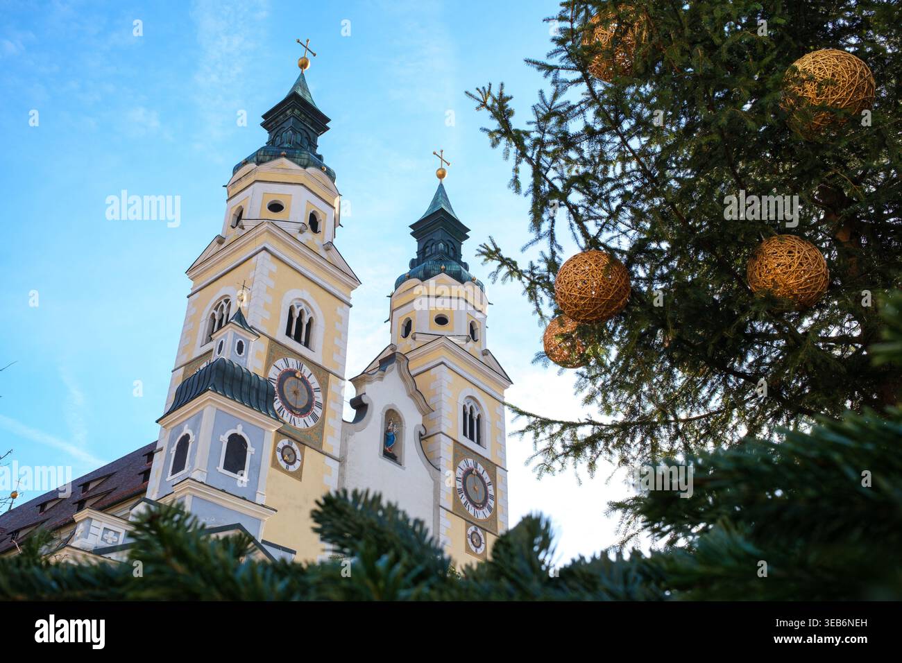 Vue sur les clochers jumeaux de la cathédrale de Brixen avec des horloges et des flèches vertes derrière un arbre de Noël décoré sous un ciel bleu dans le Trentino-South Tyr Banque D'Images