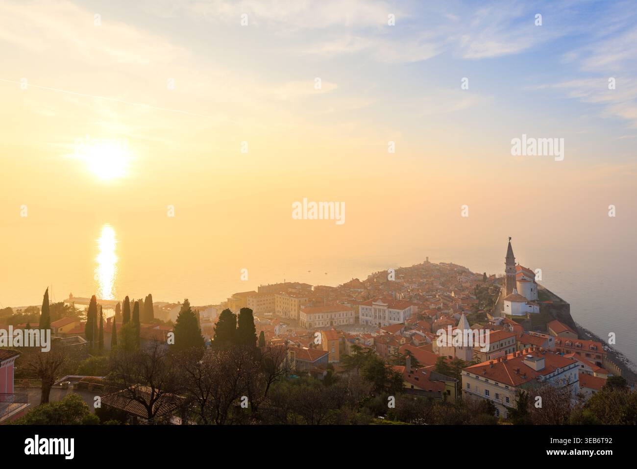 Vue sur la vieille ville historique de Piran avec ses bâtiments au toit rouge et l'église paroissiale George au coucher du soleil en Slovénie. Banque D'Images