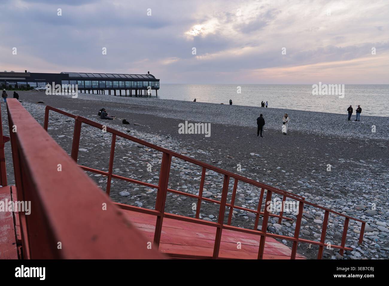 Batumi, géorgie 21 avril 2026 : les gens apprécient un coucher de soleil serein sur la plage de galets de la mer Noire à batumi, géorgie, avec un bâtiment moderne sur pilotis à proximité Banque D'Images