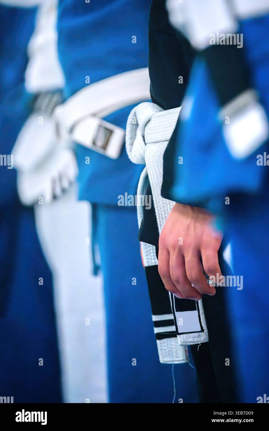Vue d'artistes martiaux debout dans une rangée portant des uniformes bleus et des ceintures blanches avec un accent sur un nœud noué et une main. Banque D'Images
