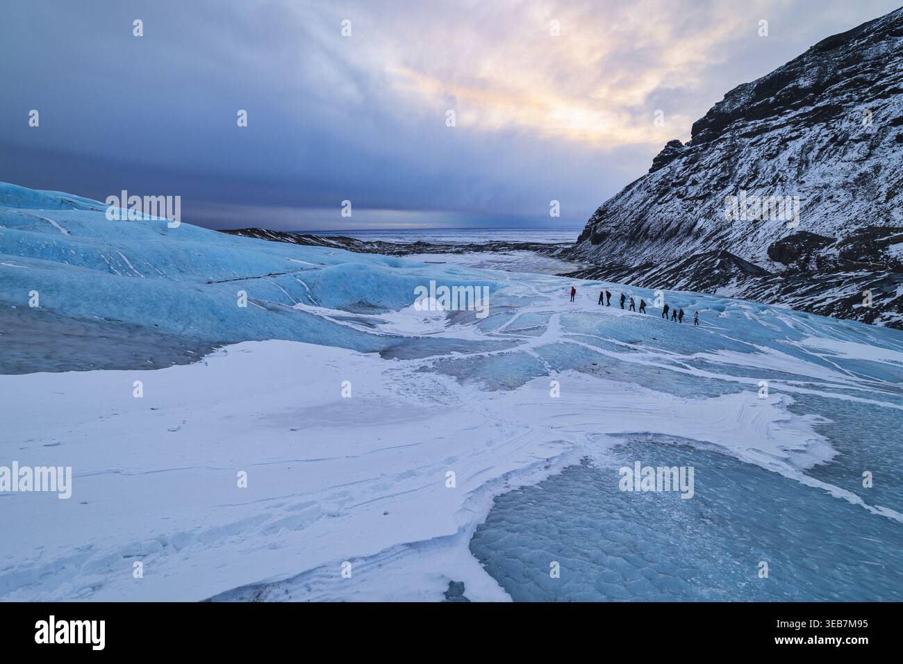 Vue de gens marchant sur la glace bleue du glacier Falljokull sous un ciel nuageux à Sveitarfelagid Hornafjordur, Islande. Banque D'Images