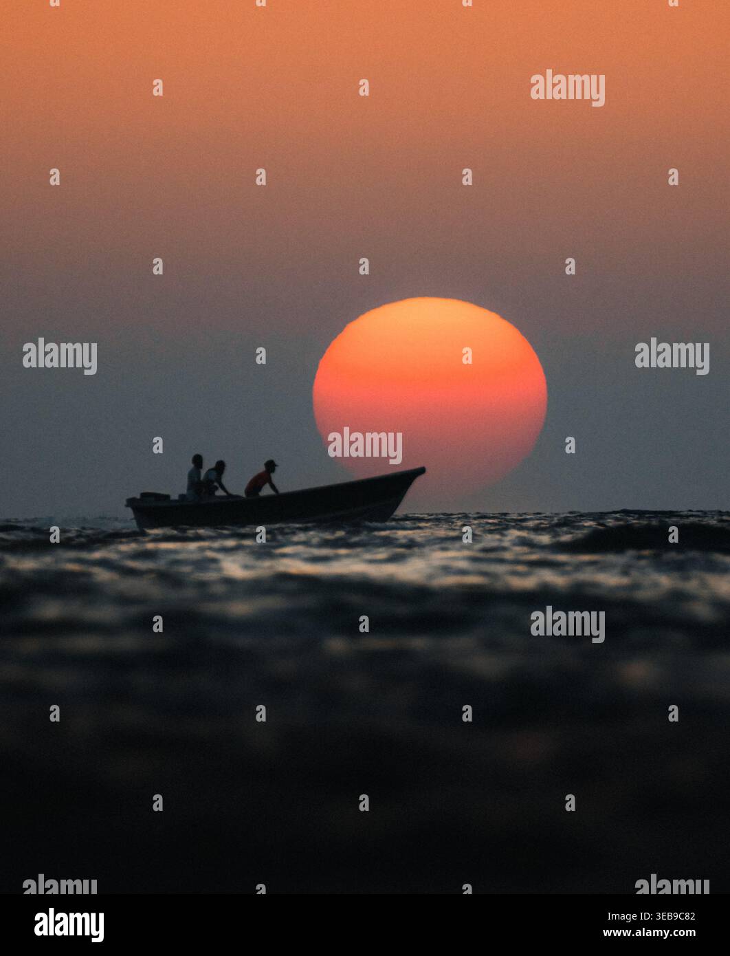 Vue de pêcheurs dans un petit bateau silhouette contre un soleil orange massif se couchant sur les vagues calmes de l'océan Baloutchistan, Pakistan. Banque D'Images