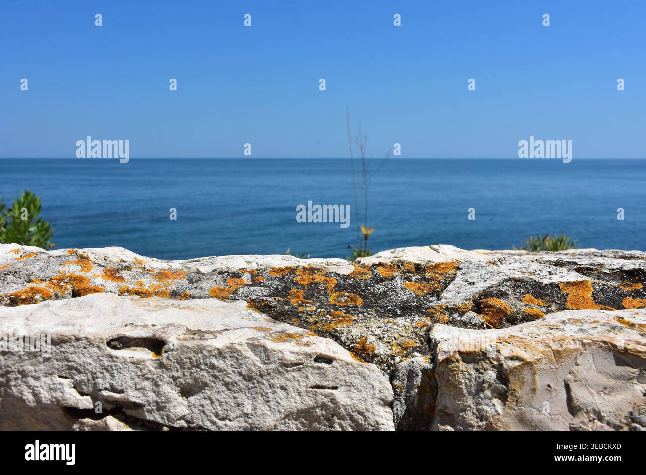 Gros plan du mur de pierre altérée avec lichen et horizon de mer flou sous un ciel bleu clair Banque D'Images
