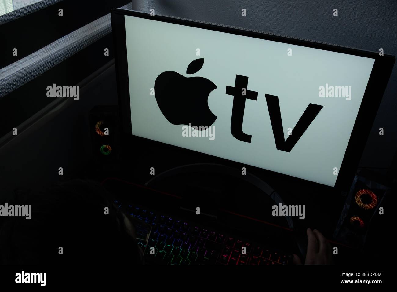 Le logo Apple TV est affiché sur un écran d'ordinateur dans un environnement de bureau à domicile faiblement éclairé Banque D'Images