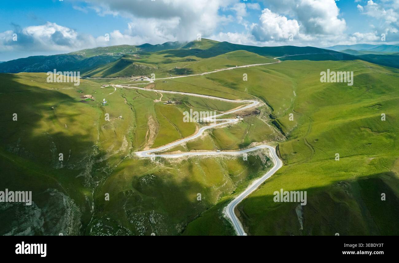 Vue panoramique sur la route de montagne sinueuse traversant des pentes verdoyantes sous un ciel lumineux Banque D'Images