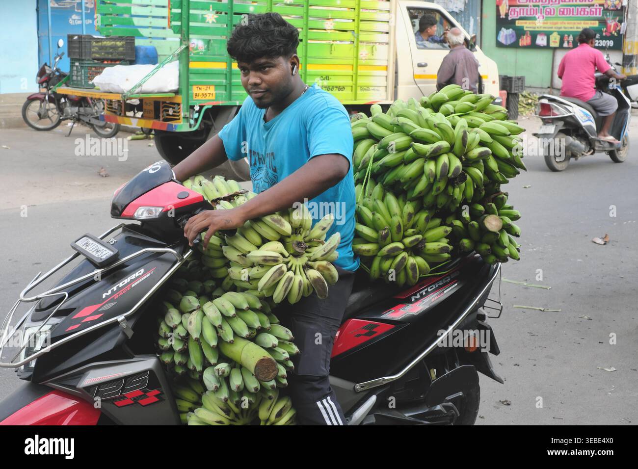 Un homme dans un marché de Kanchipuram, Tamil Nadu, Inde du Sud, part sur sa moto chargée de gros bouquets de bananes vertes Banque D'Images