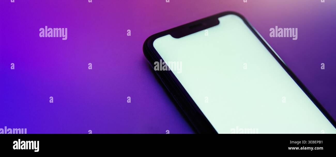 Gros plan d'un téléphone mobile moderne avec un écran blanc vide blanc, éclairé par une lumière rose néon et violette. Maquette de smartphone pour la présentation de la conception d'application avec grand espace pour votre texte. Banque D'Images