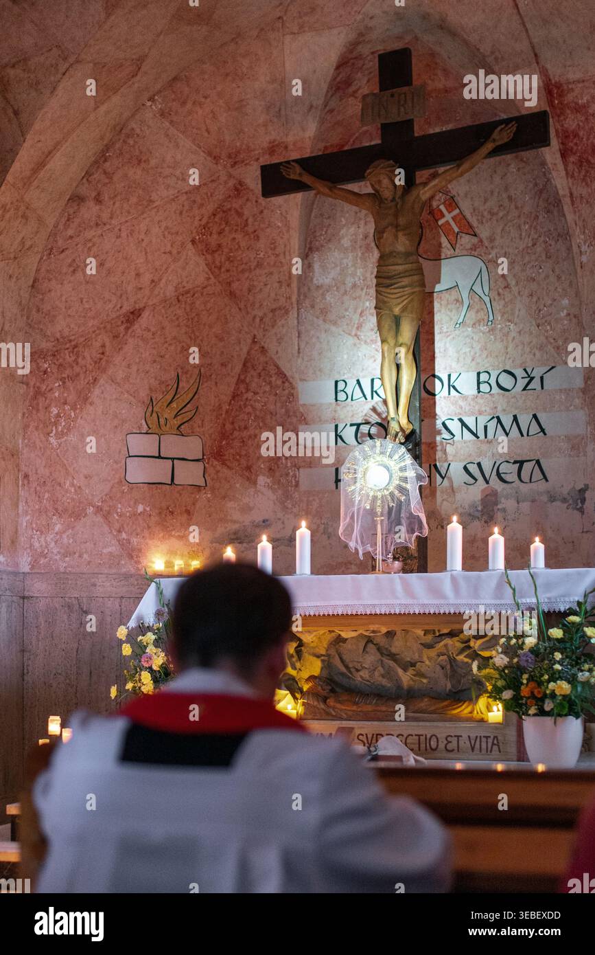 Ruzomberok, Slovaquie - 3 avril 2026 : le prêtre catholique s'agenouille en prière devant le crucifix et l'autel à l'intérieur de l'église du Calvaire pendant le service religieux. Banque D'Images