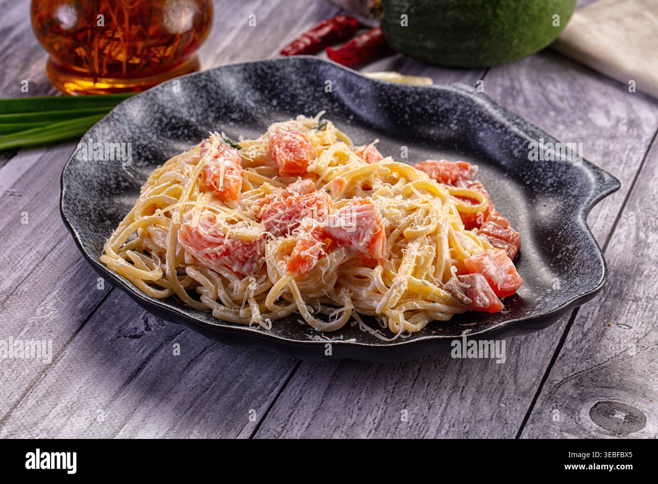 Une délicieuse assiette de spaghettis crémeux avec des morceaux de saumon et du parmesan. Le plat est présenté sur un fond en bois gris rustique avec I frais Banque D'Images