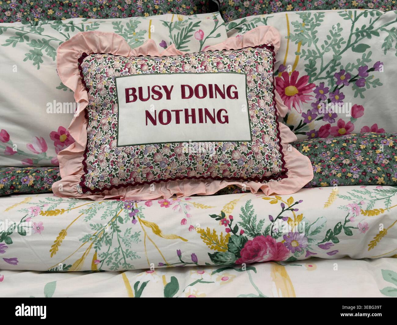 Oreiller décoratif sur lit floral avec occupé à ne rien faire de texte Banque D'Images