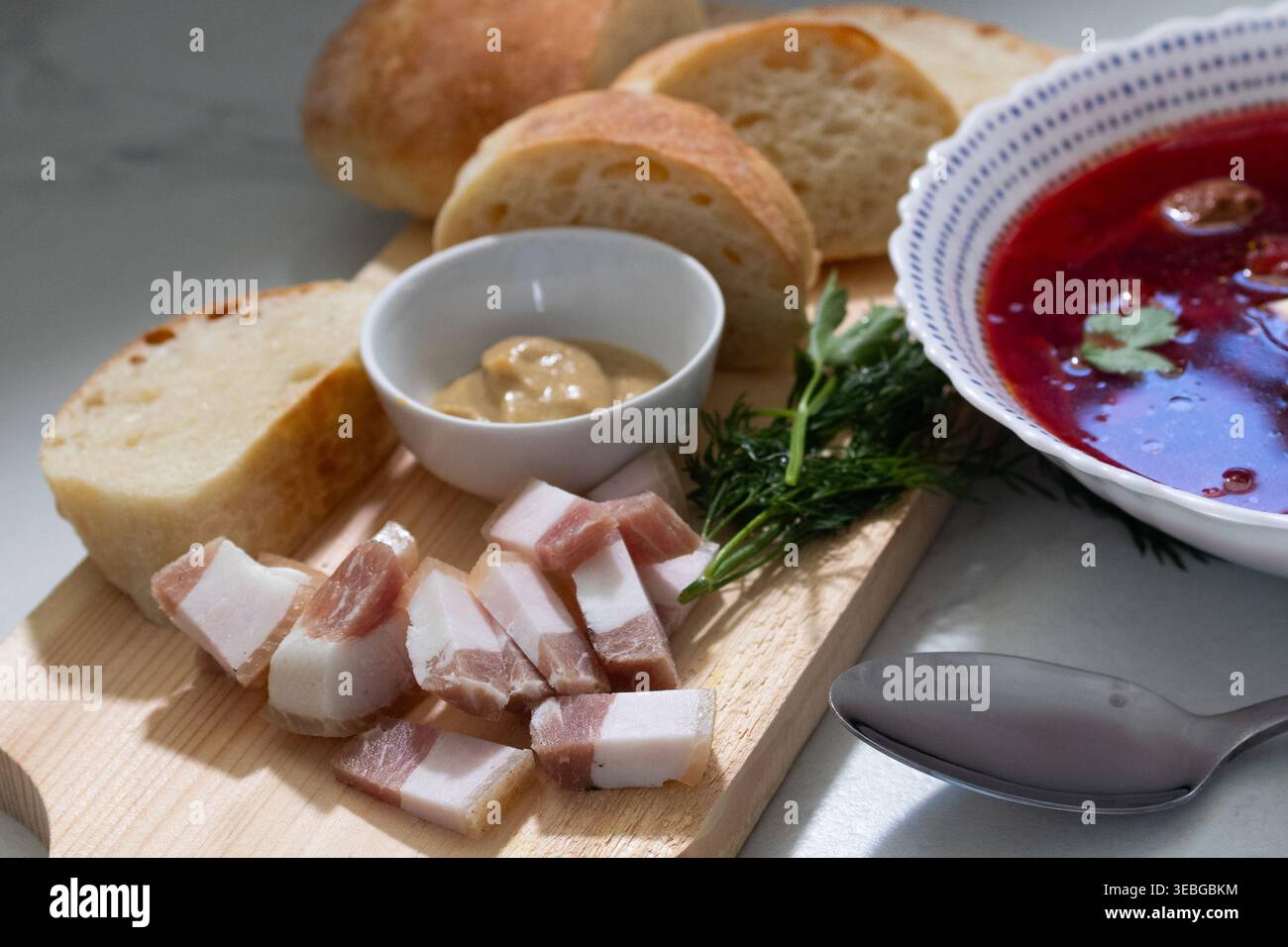 Soupe de betterave avec du saindoux et du pain sur une planche de bois. Repas slave traditionnel servi dans un bol blanc. Déjeuner maison sain avec bouillon de légumes et pain de seigle. Concept culinaire pour la conception de menu. Banque D'Images