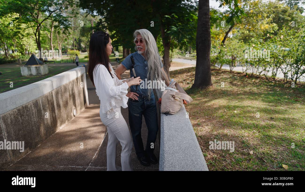 Créateur de contenu interviewe un homme âgé avec de longs cheveux blancs dans un parc, créant du contenu attrayant pour les médias sociaux Banque D'Images