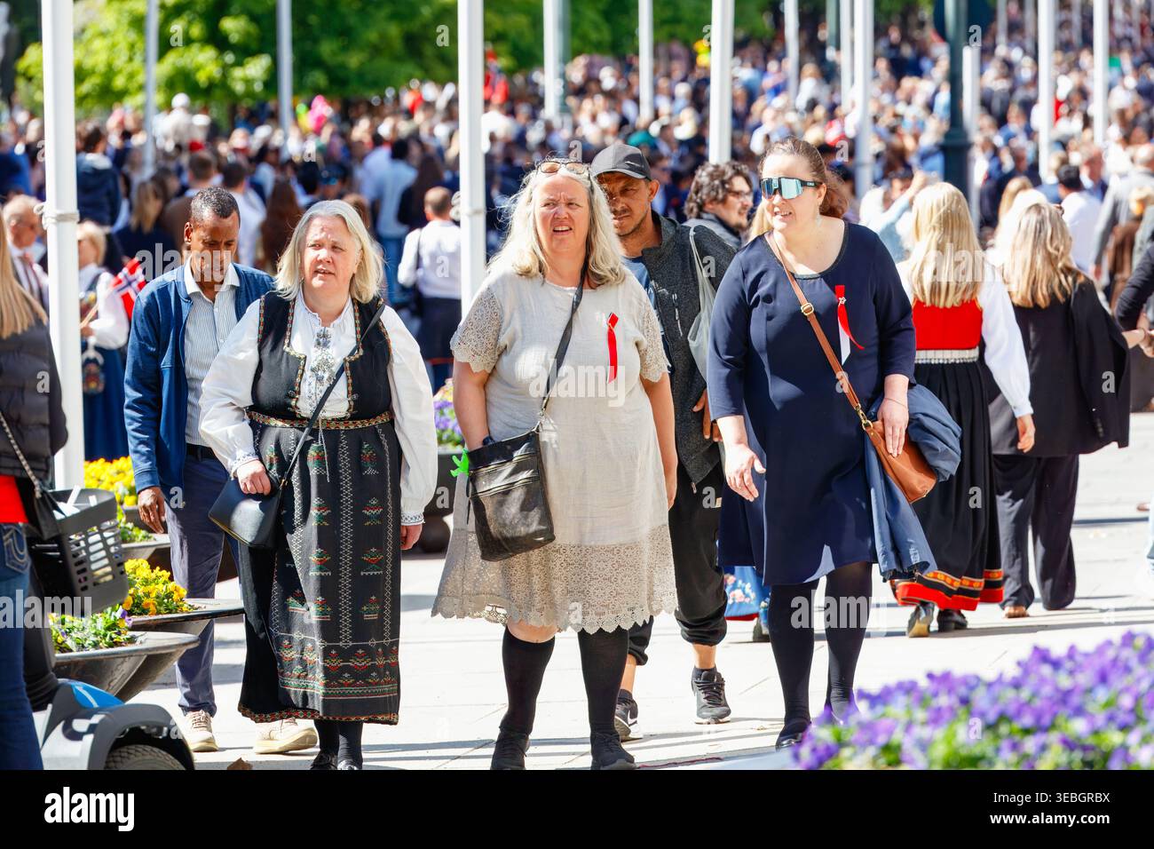 Oslo, 17 mai 2025 : des femmes en robes traditionnelles marchent le long d'une rue festive du jour de la Constitution, avec des foules, des drapeaux norvégiens et une vie urbaine élégante Banque D'Images
