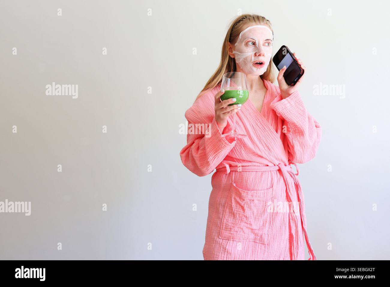 Femme en peignoir rose faisant un appel téléphonique pendant la routine de spa à la maison, scène de style de vie de bien-être. Banque D'Images