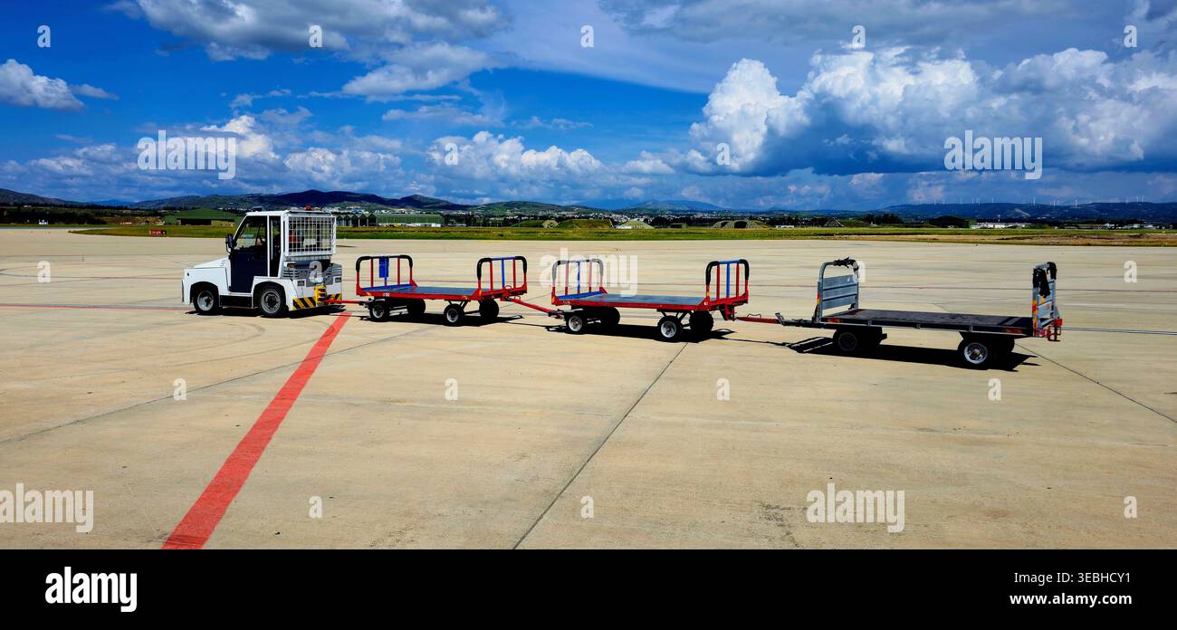 Un train de bagages vide tourne au ralenti sur le tablier blanchi par le soleil Banque D'Images