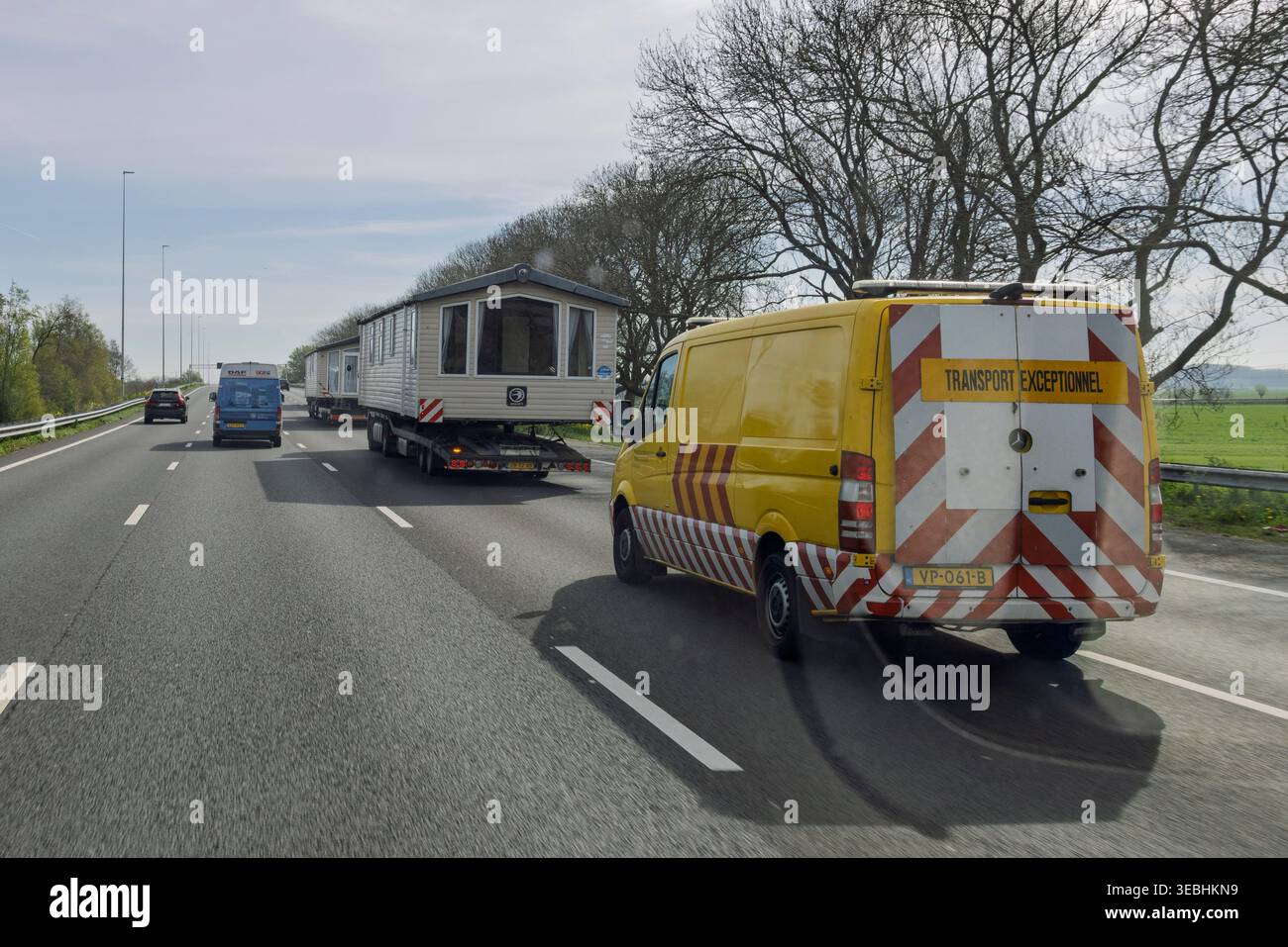 Pays-Bas, 15 avril 2026. Un véhicule d'escorte jaune suit des camions transportant des maisons préfabriquées surdimensionnées sur une autoroute néerlandaise, marquée transport Banque D'Images