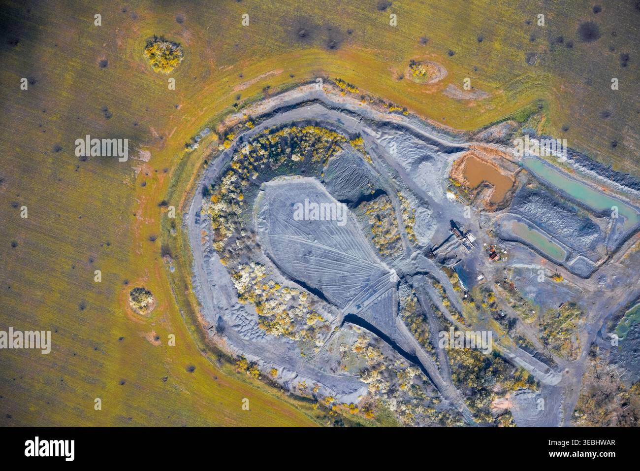 Impact environnemental montrant une érosion sévère du sol, des pistes de machines et des bassins de boue toxiques dans une carrière industrielle massive contrastant fortement avec le reste de la prairie verte. Banque D'Images