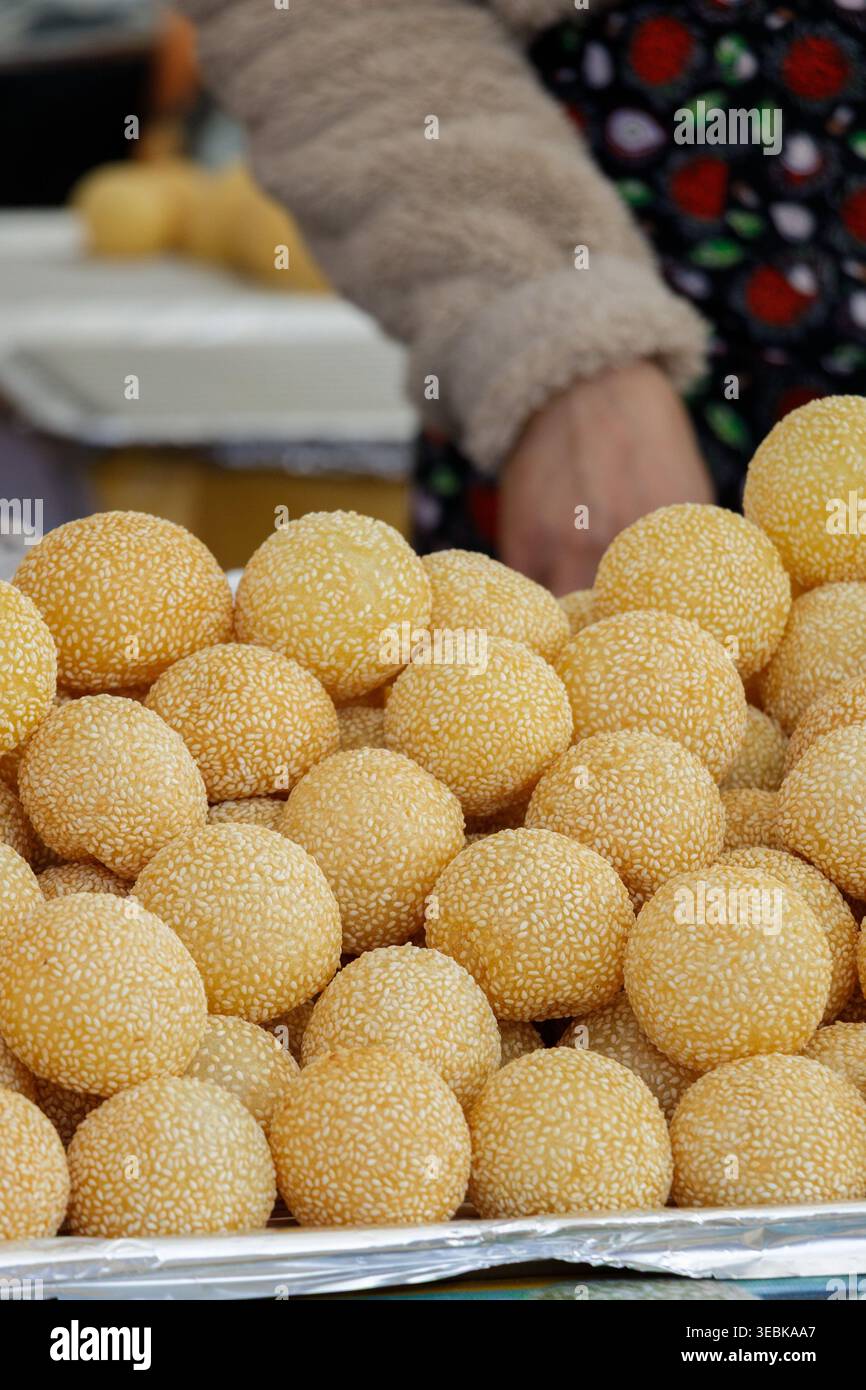 Gâteries au sésame doré. Vendeur du marché organisant soigneusement des boules de sésame artisanales pour l'affichage du festival Banque D'Images