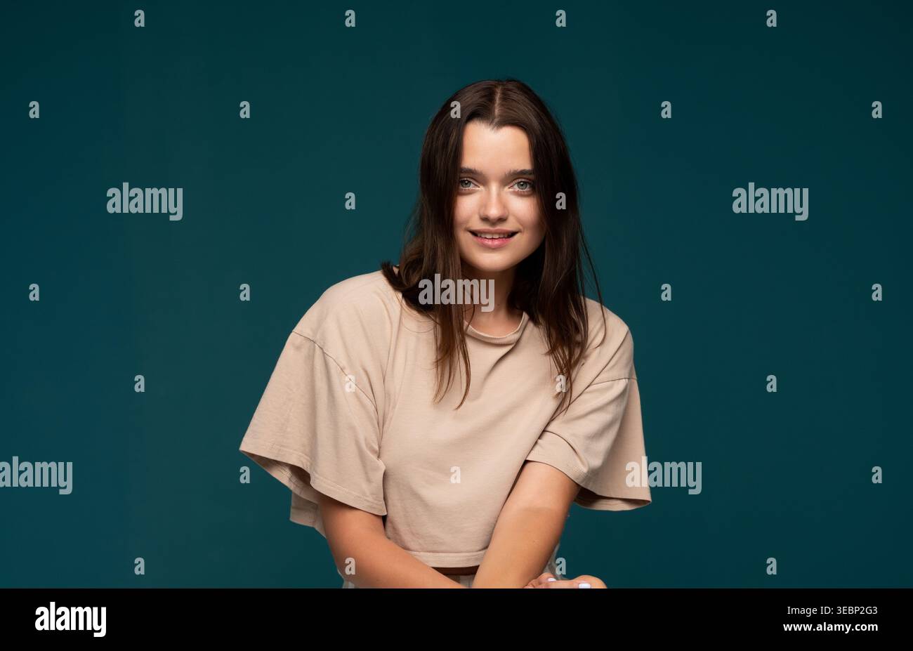 Jeune femme avec une beauté naturelle souriante sur fond bleu sarcelle, style décontracté et expression authentique Banque D'Images