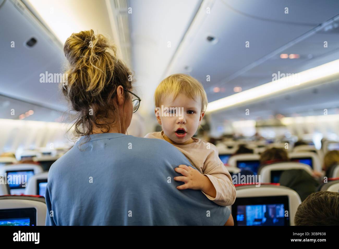 Maman calmant l'enfant bouleversé pendant le vol familial en voyageant dans l'avion. Banque D'Images