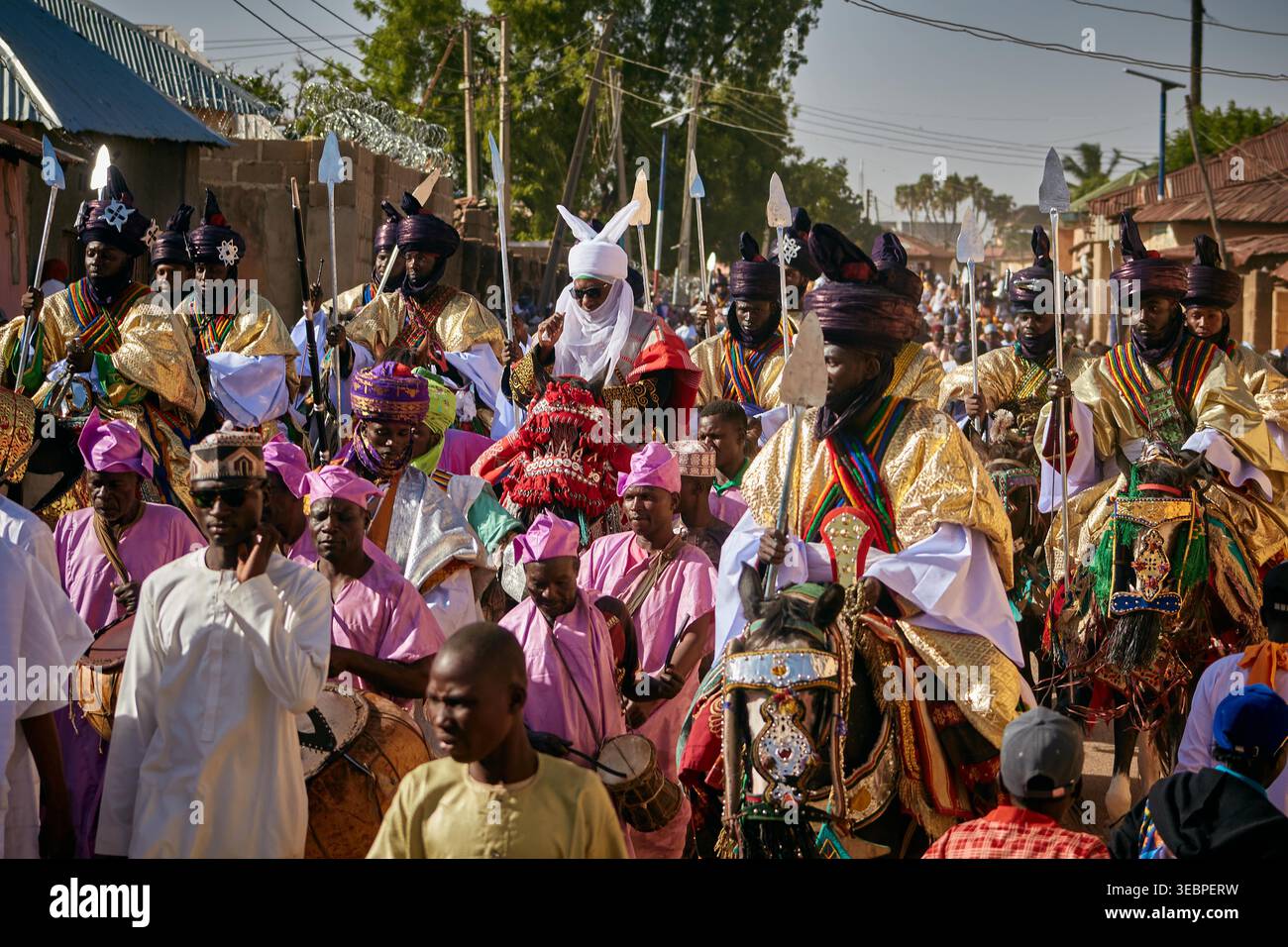 Zaria City, Nigeria - 22 mars 2026 : vue d'une procession cérémonielle vibrante de cavaliers dans une tenue dorée resplendissante et d'une foule en rose vif, animée Banque D'Images