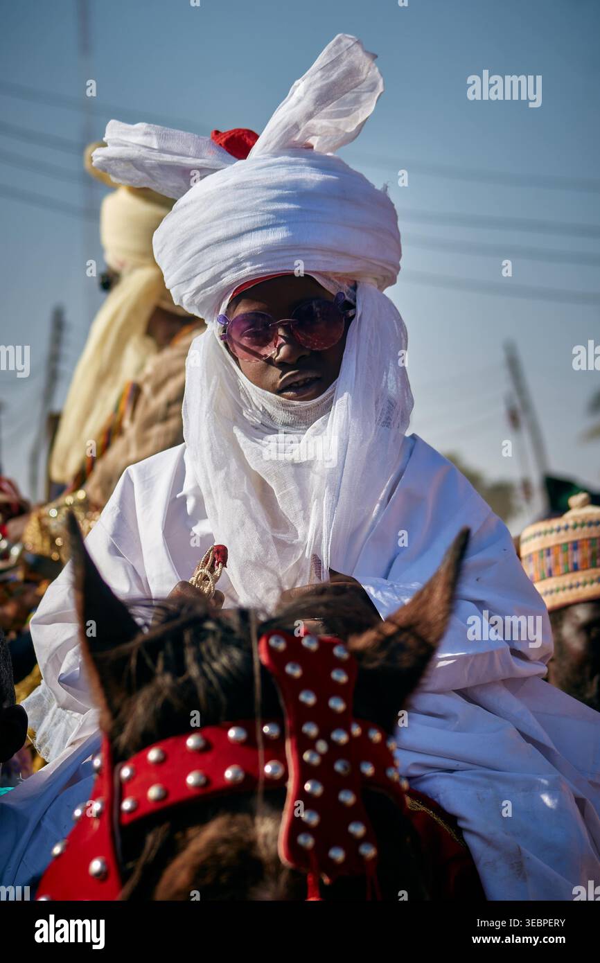 Zaria, Nigérian - 22 mars 2026 : vue d'une figure royale dans une tenue blanche brillante et des nuances sombres, montée sur un cheval sombre avec un t rouge frappant Banque D'Images