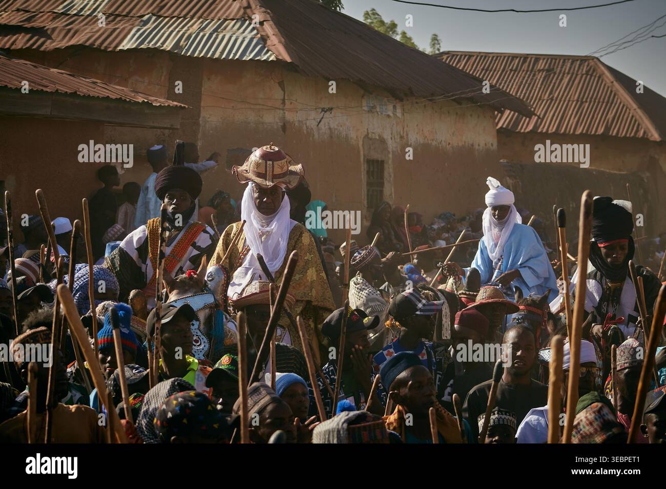 Zaria, Nigeria - 22 mars 2026 : vue d'hommes à la décoration traditionnelle, leurs robes riches et leur personnel contrastant avec les murs texturés et cuits au soleil des maisons Banque D'Images