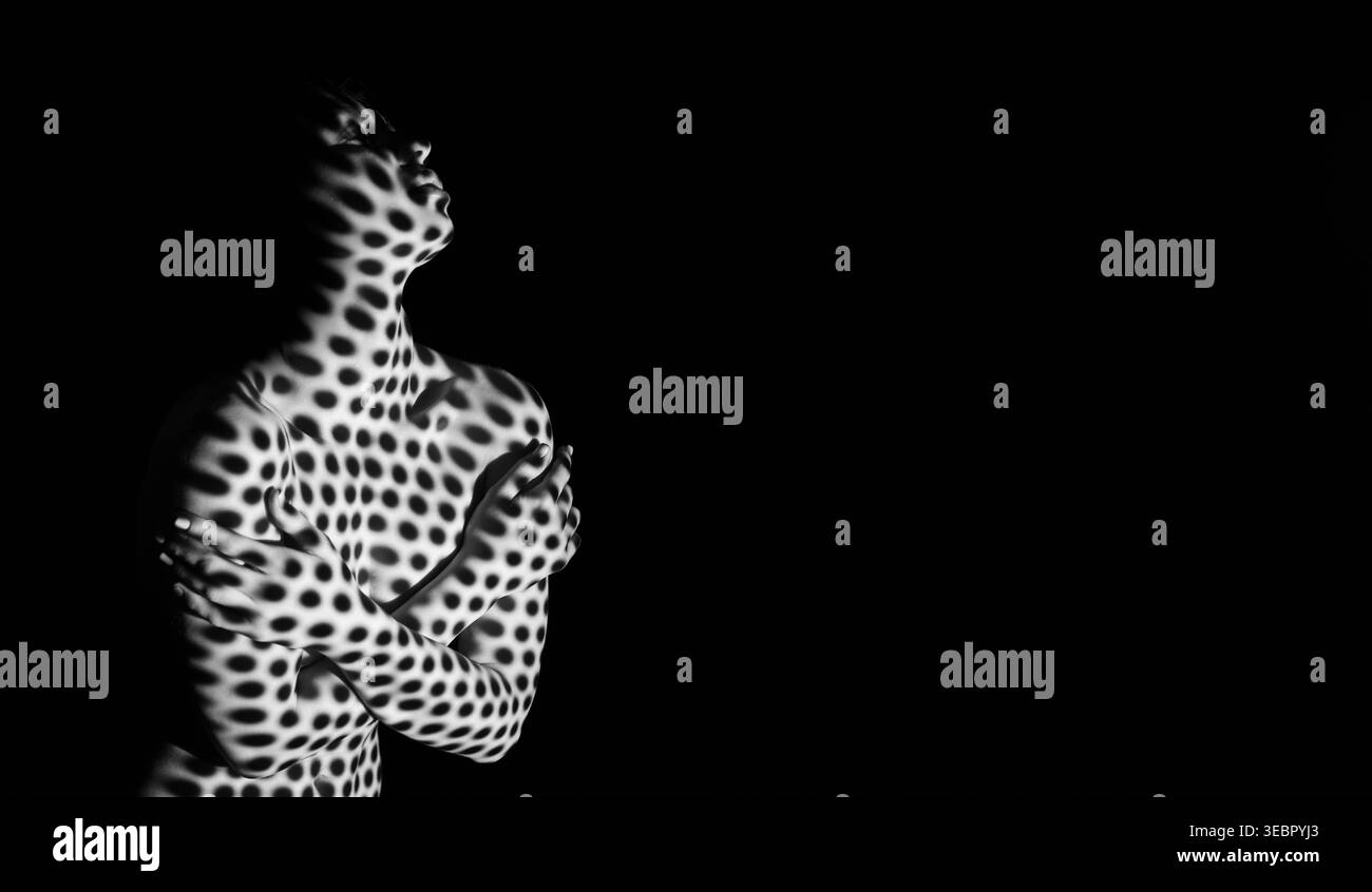Femme posant avec un effet d'éclairage à pois dramatique sur un fond noir Banque D'Images
