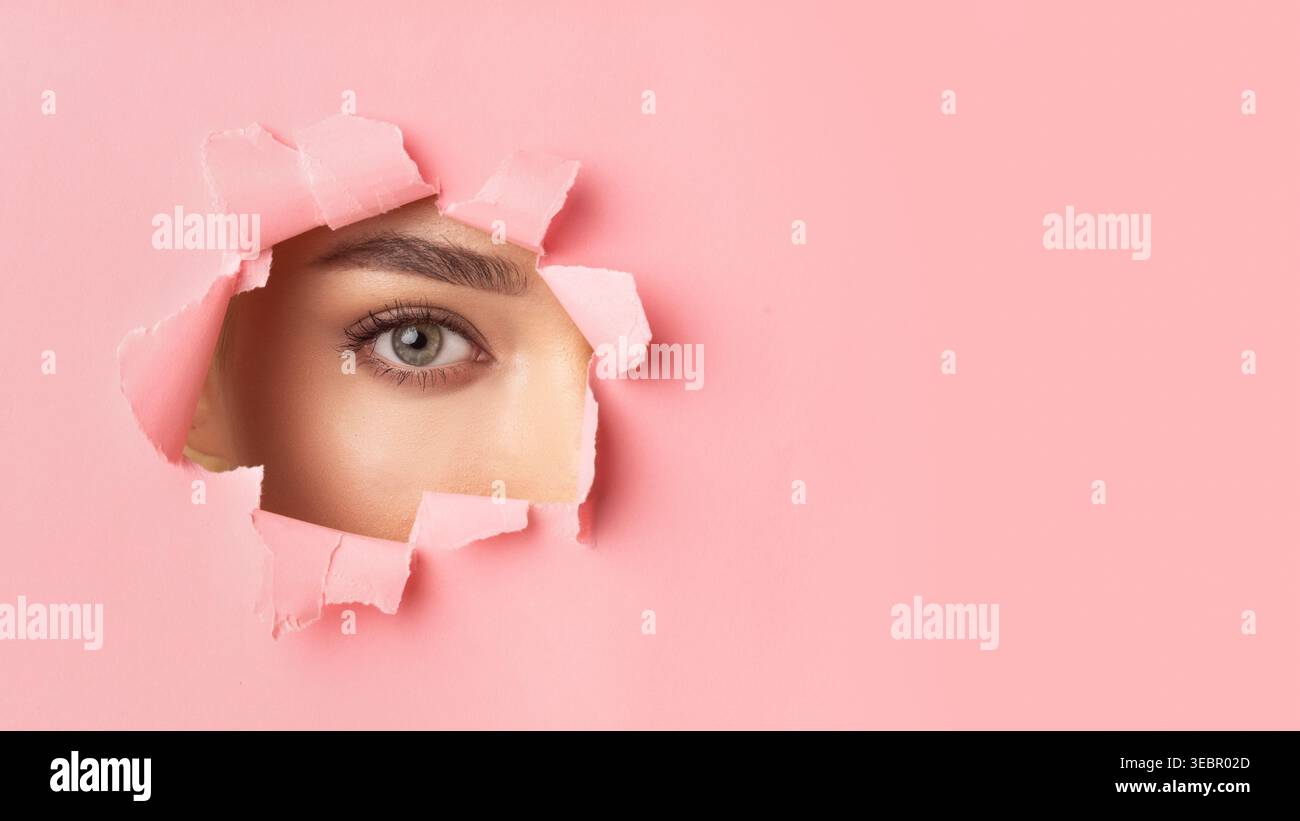 Regard regardant à travers un mur rose déchiré révélant un gros plan du visage d'une femme Banque D'Images