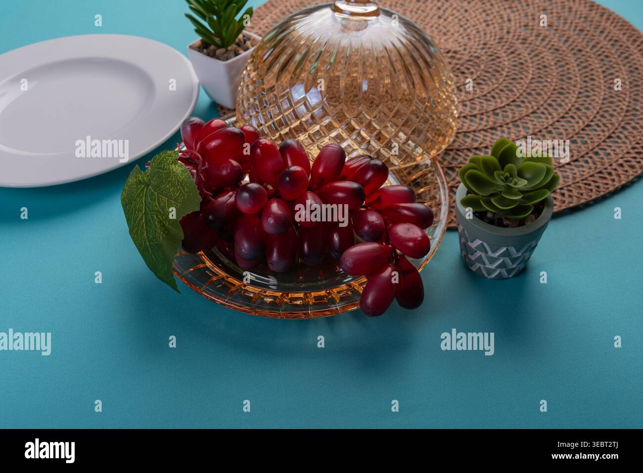 Still Life présente des raisins rouges sur plat en verre, complétés par des plantes succulentes. La composition met en valeur des textures douces, un éclairage équilibré et une palette Banque D'Images