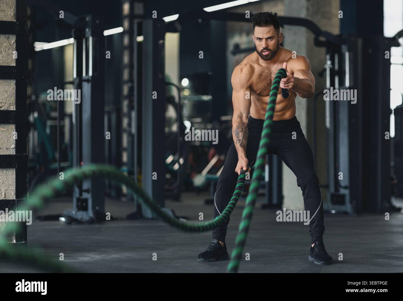 Fit Man Training avec des cordes de combat dans Modern Gym pendant la séance d'entraînement de jour Banque D'Images