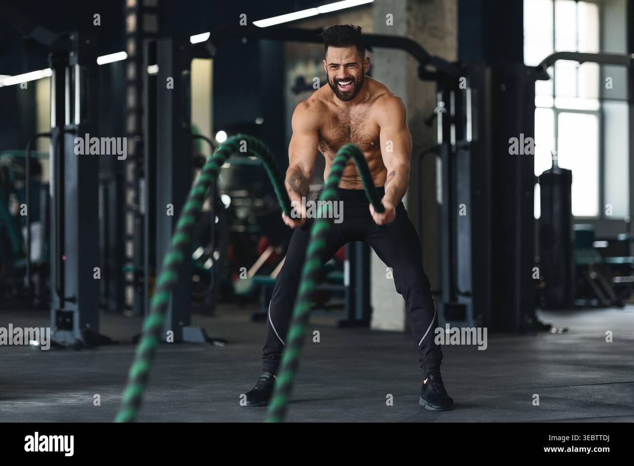 L'homme exerce avec des cordes de combat dans un gymnase moderne pendant la session d'entraînement de jour Banque D'Images