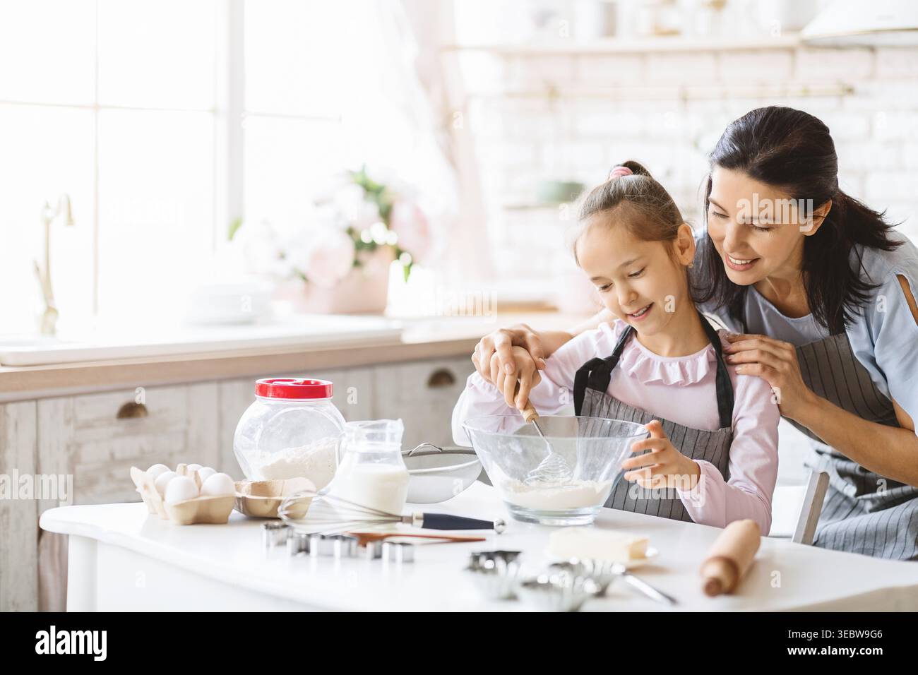Mère et fille appréciant cuisiner ensemble dans une cuisine lumineuse tout en préparant une recette Banque D'Images