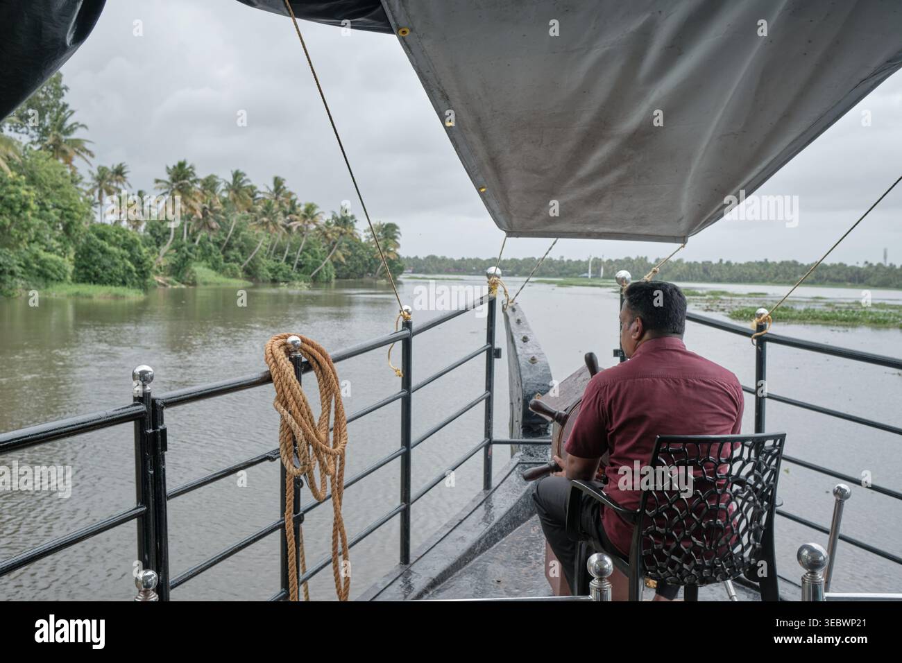 La vue arrière d'un capitaine à la barre d'une péniche naviguant sur les eaux pittoresques de Kumarakom, Kerala, Inde. Banque D'Images