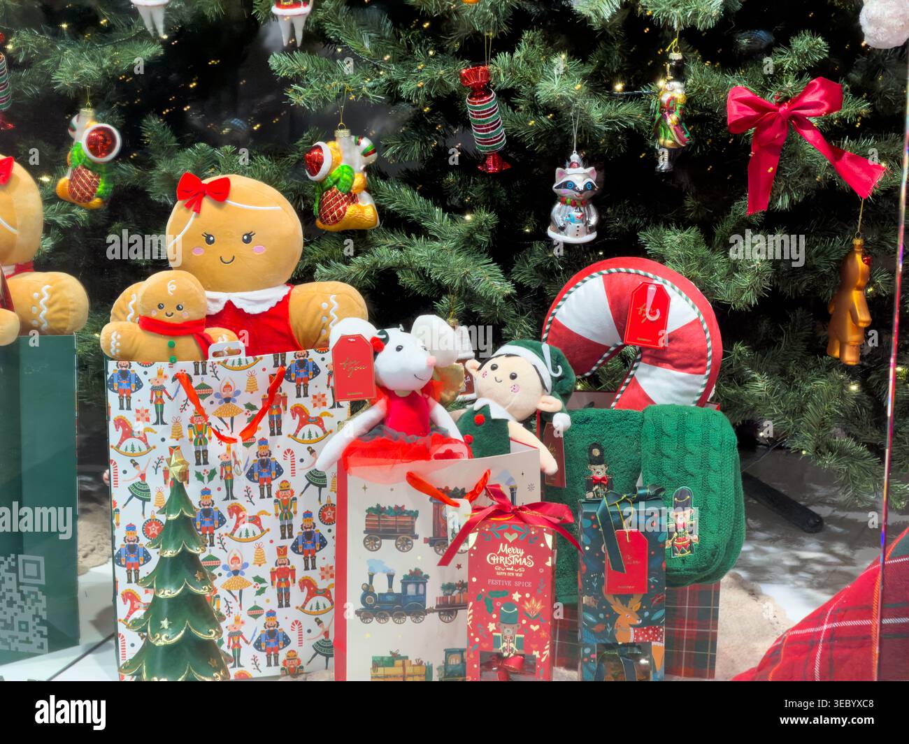 Figurines en pain d'épice en peluche et jouets en peluche, avec canne à bonbons et boîtes cadeaux, sont exposés sous un sapin de Noël, évoquant la chaleur et les achats festifs Banque D'Images