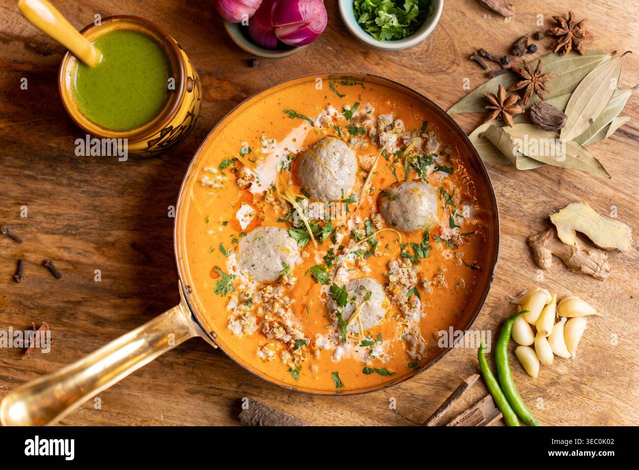 Ce cliché au-dessus de la tête présente un curry de boulettes de viande indien éclatant baigné d'une délicieuse sauce à l'orange crémeuse. Il est magnifiquement arrangé avec des herbes fraîches Banque D'Images