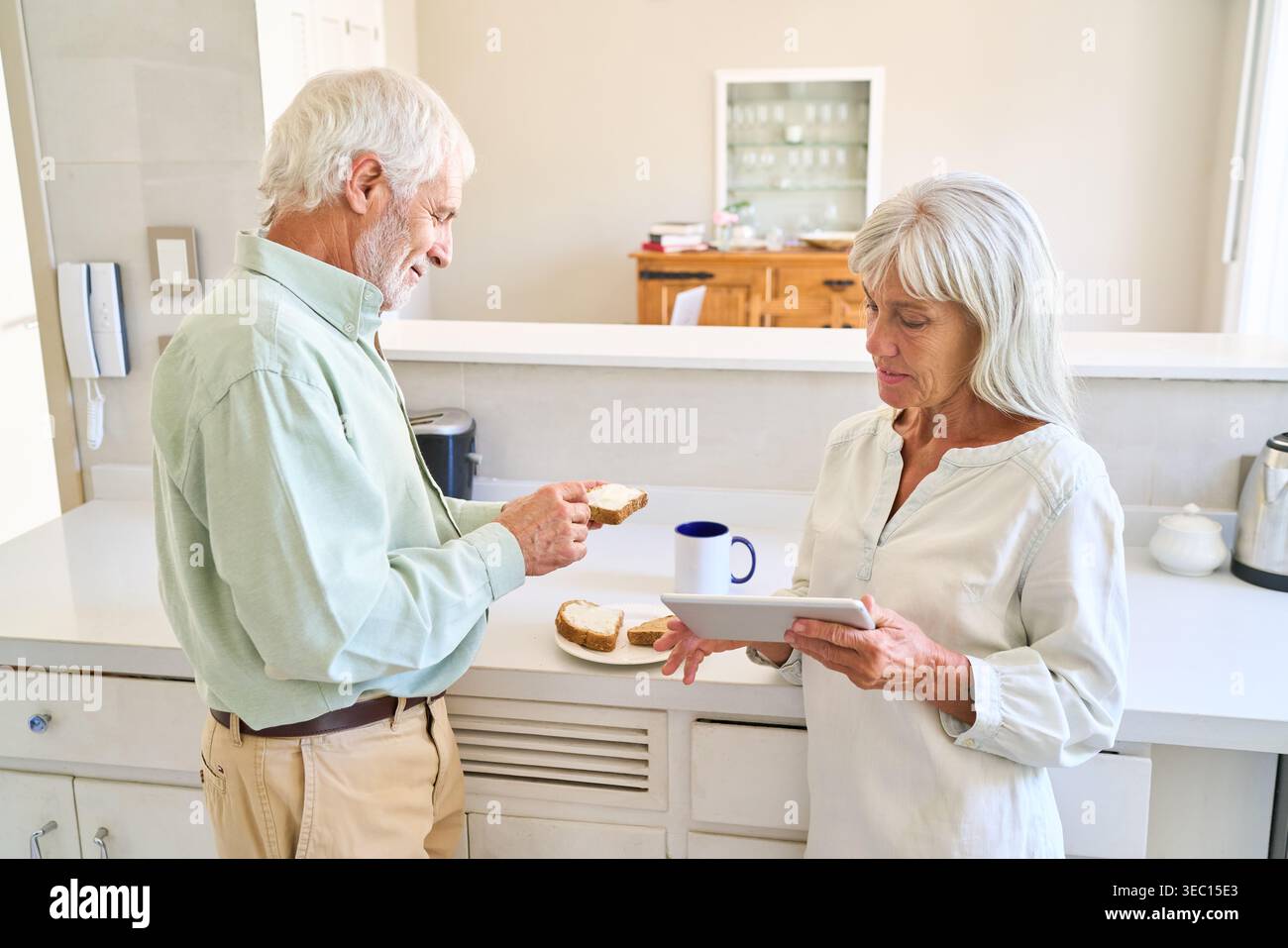 Vieillissement en bonne santé et inclusion numérique — un couple de personnes âgées profite d’un petit-déjeuner détendu dans leur cuisine lumineuse. Banque D'Images
