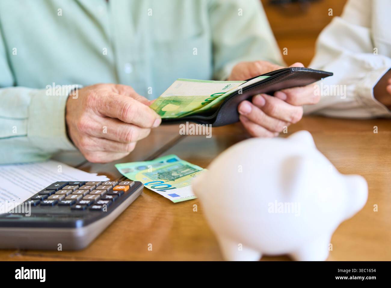 Planification de la retraite et sécurité financière. Une personne senior est vue gérer son épargne, tenant un portefeuille avec des billets en euros, avec une tirelire an Banque D'Images