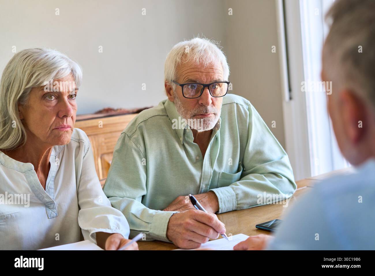 Planification de la retraite et protection financière — un couple de personnes âgées est engagé dans une discussion sérieuse avec un conseiller financier, examinant les documents pour es Banque D'Images