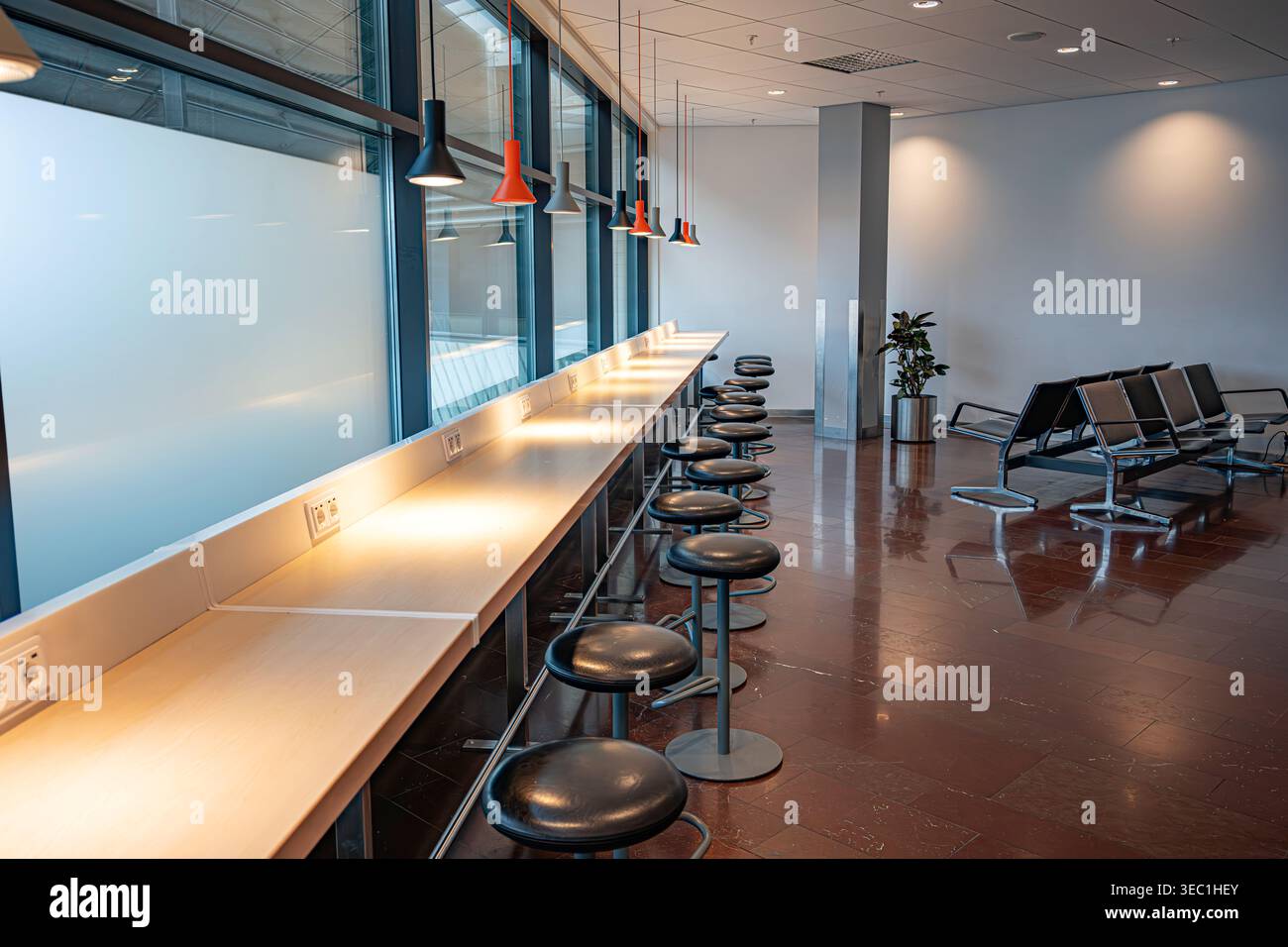 Le salon minimaliste de l'aéroport est doté d'un long comptoir de travail en bois avec prises de courant et de tabourets de bar noirs sous des lampes suspendues. Banque D'Images